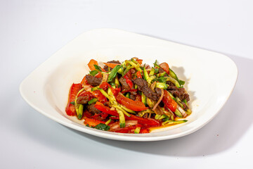 Salad of fried vegetables and beef with tomatoes and onions is on the plate