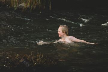 Boy swimming in fresh water river with at dusk in New South Wales, Australia