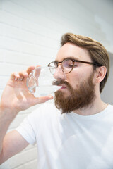 Young bearded man drinking water from a glass. Healthy lifestyle concept.