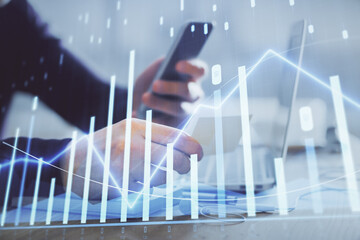 Double exposure of man's hands holding and using a phone and financial graph drawing. Analysis concept.