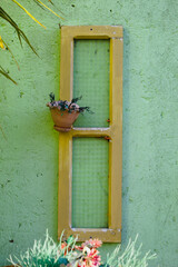 Janela de madeira com vaso de flores e parede verde.