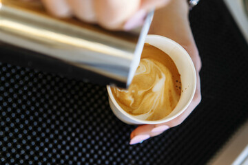 Barista draws milk over a coffee - making latte art for cappuccino