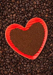 Ground coffee in red heart shape plate on fresh coffee beans background.