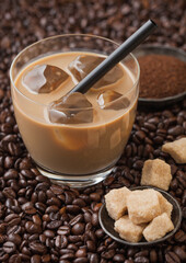 Glass of cold coffee with ice cubes and straw on fresh raw coffee beans with cane sugar and powder.