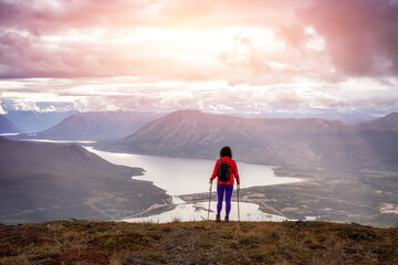 Adventurous Girl Hiking up the Nares Mountain during a cloudy and sunny evening. Taken at Carcross, near Whitehorse, Yukon, Canada. - obrazy, fototapety, plakaty