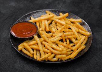 French fries chips with tomato ketchup in black plate on dark table background.