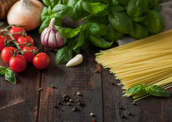 Raw spaghetti pasta in glass bowl with oil and garlic, basil and tomatoes with pepper and onion on wooden background