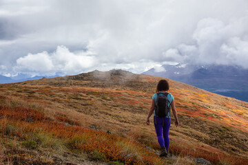 Adventurous Girl Hiking up the Nares Mountain during a cloudy and sunny evening. Taken at Carcross, near Whitehorse, Yukon, Canada.