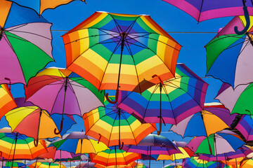 Fototapeta na wymiar Rainbow Colored Umbrellas Hanging On The Background Of A Blue Sky