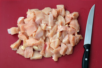 Chicken raw meat cut into pieces top view. Pink meat on a red plastic cutting board and a knife. Chopped raw meat piled up in a bunch.