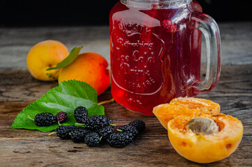 Homemade, rustic compote of apricot and mulberry in a glass with a straw on old wooden boards.
