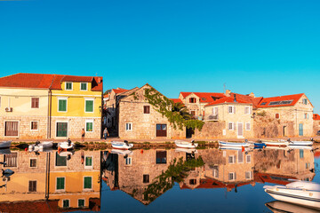 Fototapeta na wymiar Vrboska village embankment, houses are reflected in the water. Hvar island, Croatia.