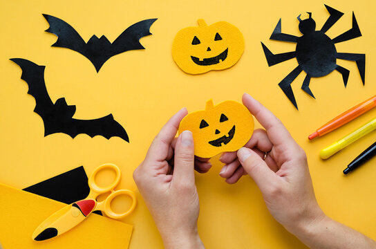 female hands making, sewing, painting halloween decorations. handmade pumpkin, black bat, spider on orange background. preparation for terrible holiday.