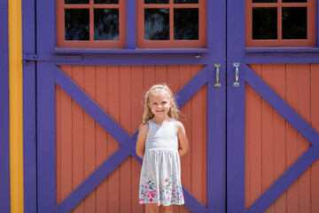 Cute little girl standing in front of colorful barn doors © Kristen