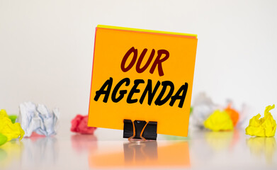 Sticky note writing Our Agenda on Office table with keyboard, dice, pen, compass