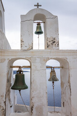 Obraz premium Close-up of a rustic old bell tower in Oia, Santorini island with mediterranean sea background on a cloudy day.