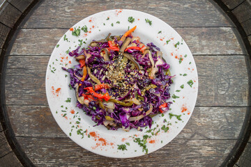 Vegetarian and healthy food. Sauteed vegetables, spices and seeds on white plate. Rustic wood table.