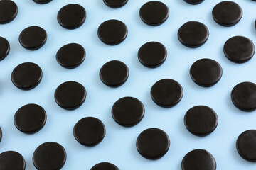 Black licorice candy coins in rows on light blue background