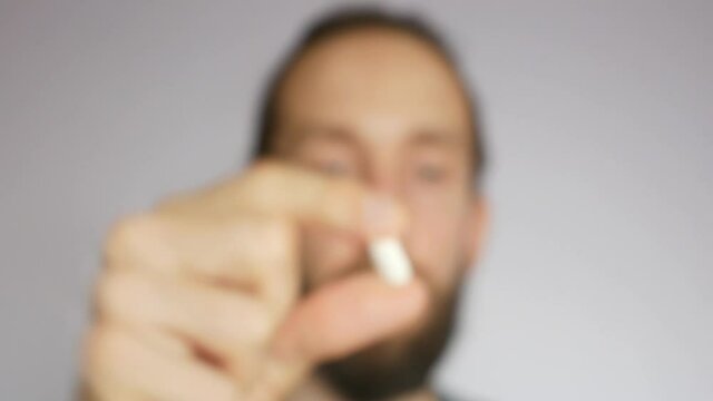 A young bearded man takes an elongated pill