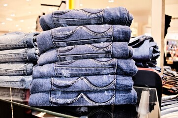 Stacked of folded jeans in store on wooden shelf.