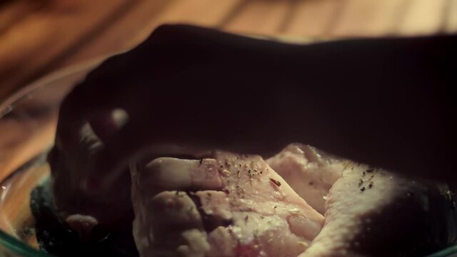 Hand Sprinkle Dried Herbs And Spices To Add Flavor On The Chicken Legs At The Microwavable Glassware. - Close Up Shot