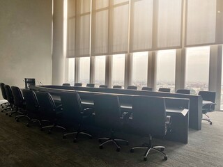 An empty meeting room have to full frame window with a curtain shading down. A black table and many chairs with wheel. Located at the tall building, see the top city view. Nobody in business area