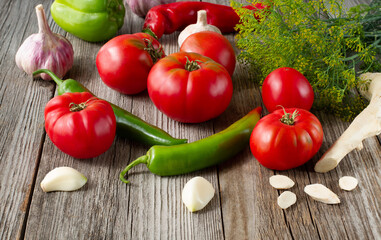 Tomatoes, garlic, dill, horseradish, hot peppers lie on a wooden table. Healthy food concept.