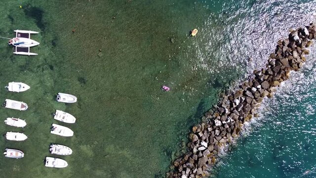 Bird eye aerial view for speed boats and yachts at the sea and small rocky shore with sun light reflections. Castiglioncello bay. Livorno, Tuscany. Italy. Summer season.