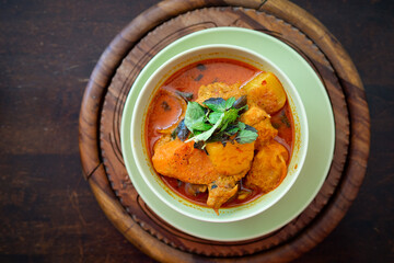 Chicken curry in a green bowl on a wooden base background.