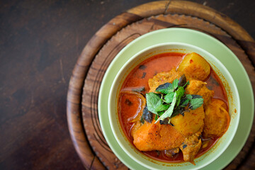 Chicken curry in a green bowl on a wooden base background.