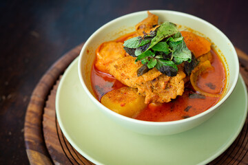 Chicken curry in a green bowl on a wooden base background.