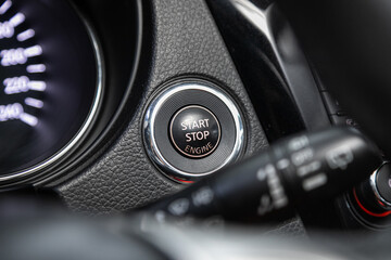 Car dashboard:  black engine start stop button, car interior details. Soft focus..