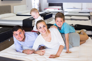 Man with woman and children are testing quality of mattress in store.