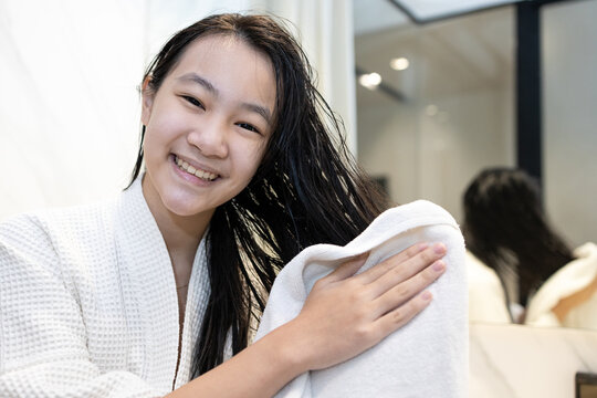 Asian Child Girl In White Bathrobe,using A Towel To Wiping Her Long Black Hair After Washing Her Hair,female Holding With White Towel Wipe Head In The Bathroom After Shower,hair And Scalp Care Concept