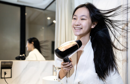 Smiling Asian Child Girl Drying Hair With Hairdryer,beautiful Woman In Bathrobe Blow Drying With Hair Dryer After Hair Washing,stand In Front Of The Mirror In Bathroom,daily Routine, Lifestyle.