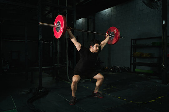 Fit muscular sport male bodybuilder workouts snatch lifting with barbells training exercise in gym fitness for a healthy lifestyle