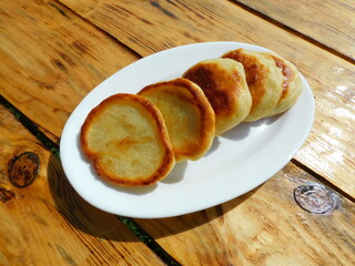 
Fried pancakes on a white plate that stands on a wooden table
