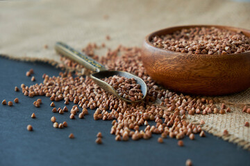 Buckwheat groats in a wooden bowl and vintage scoop. Close up on a black background. copy space for...
