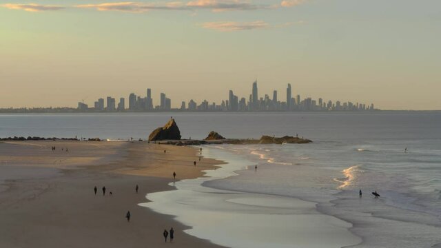 People Walking And Surfing At Currumbin Beach On Sunset - Currumbin Alley And Surfers Paradise High Rise Buildings - View From The Elephant Rock Lookout - Gold Coast, QLD, Australia. - wide shot