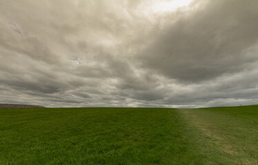 Fototapeta premium Dark stormy clouds over a green grass field