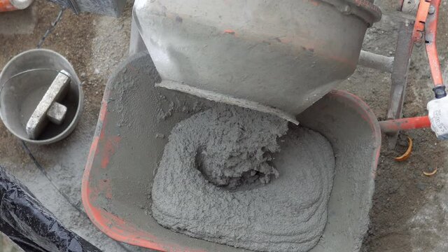 Concrete mixer pouring wet cement into wheelbarrow. A close up image of an electric concrete mixer pouring wet cement into wheelbarrow