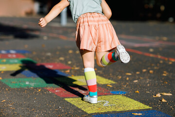 Closeup of leggs of little toddler girl playing hopscotch game drawn with colorful chalks on...