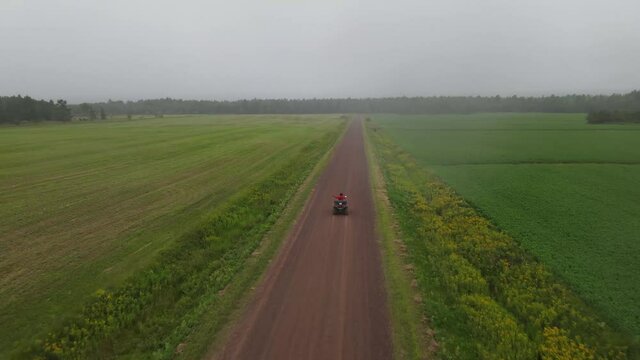 Drone flying in front of a four wheeler racing on a dirt road. Aerial view of a person driving all terrain vehicle (atv) on a dirt road and having fun in the nature. Farm field with a dirt path.