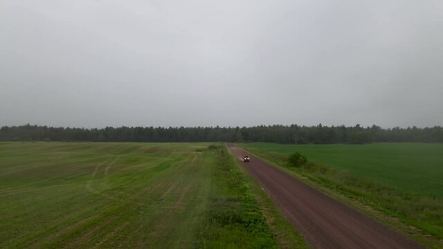 Drone flying in front of a four-wheeler racing on a dirt road. Aerial view of a person driving an all-terrain vehicles (ATV) on a dirt road and having fun in nature. Farm field with a dirt path.