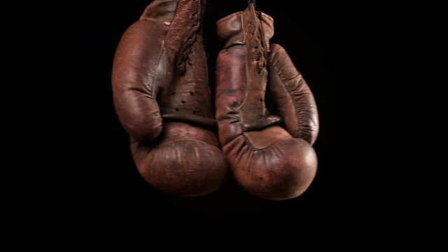 pair of leather vintage brown boxing gloves hanging on black background, slow motion