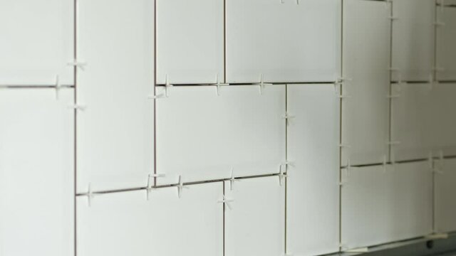 Working tiler laying white ceramic tile in a herringbone pattern on wall in kitchen.