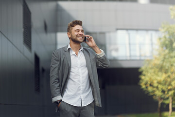 Handsome businessman in a suit and talking on the phone on the street. Portrait of a young man in business style smiling and laughing.