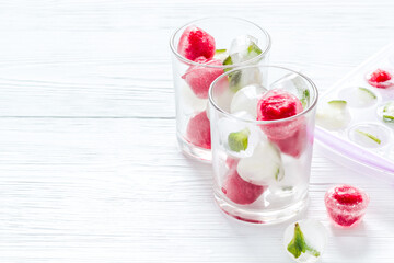 Cocktail glasses with berries in ice cubes on white table copy space