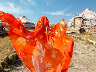 Young asian girl wearing traditional tribal cloth and scarves running in village with tents in the desert in Inner Mongolia. Fashion travel or trip concept photo red tribal scarf with gold decorations