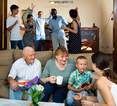 Portrait of friendly large multiethnic family celebrating together at home, talking and dancing in cozy living room..